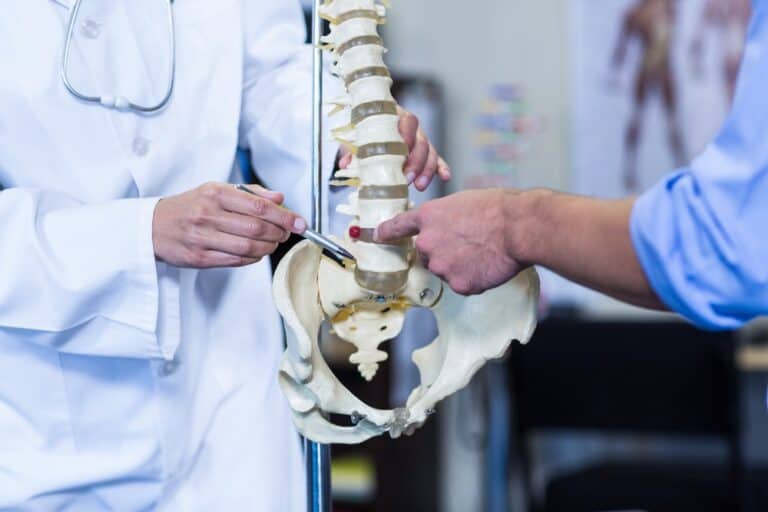 DOCTOR EXPLAINING DISC HERNIATIONS TO A PATIENT USING A SKELETON MODEL